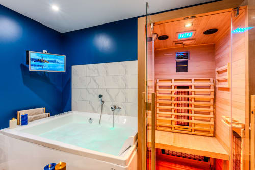 Luxury spa bathroom at Wellkhome Bordeaux with blue walls, marble tiling, illuminated sauna, and jetted tub
