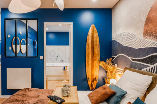 Modern bedroom with vibrant blue walls, wooden surfboard decor, and ensuite bathroom at Wellkhome Bordeaux