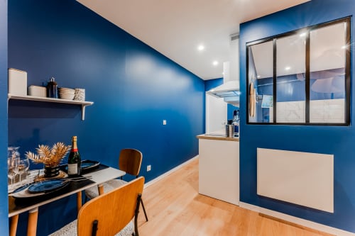 Modern blue Bordeaux apartment with dining area, kitchen window, wooden chairs, champagne bottle, and contemporary design