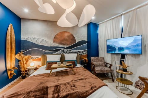 Luxury Bordeaux apartment with blue walls, brown bed, modern white ceiling lights, surfboard, mountain artwork, and