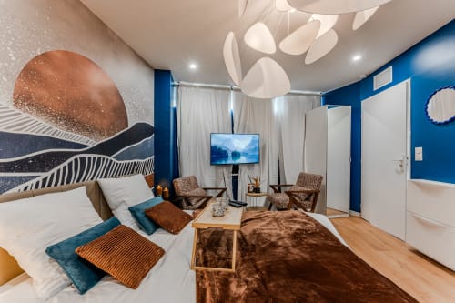 Modern Bordeaux apartment with blue walls, contemporary art, comfortable seating, wooden floor, and mounted TV.