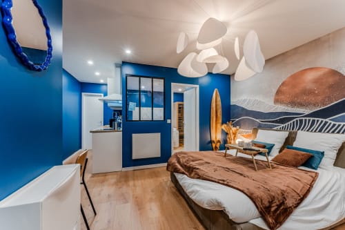 Luxury apartment at Wellkhome Bordeaux with blue walls, modern white ceiling light, bed with brown throw, and contemporary