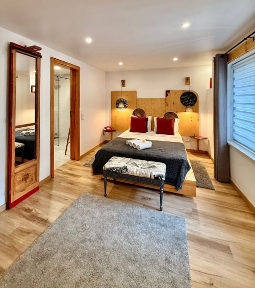 Quarto moderno na Kindnessmoon BnB em Óbidos, Portugal, com cabeceira de madeira, almofadas vermelhas e casa de banho privativa.