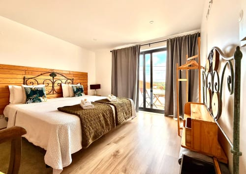 Quarto luminoso com cama de madeira, varanda com vista para a cidade e bicicleta de madeira como decoração na Kindnessmoon em Óbidos, Portugal