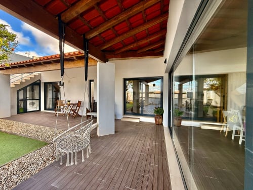 Spacious patio with wood decking, swing, white columns, and glass doors overlooking garden at Kindnessmoon cottage in Óbidos,