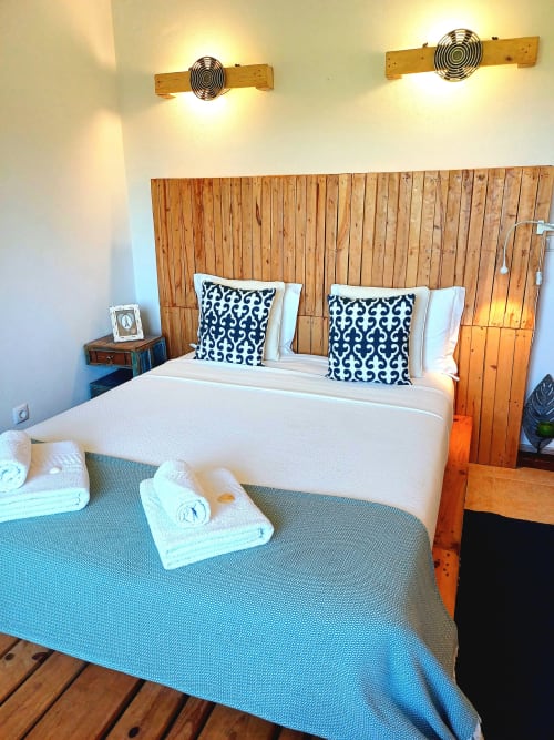 Modern bedroom in Obidos villa with wooden headboard, patterned pillows, white bedding, rolled towels, and decorative wall