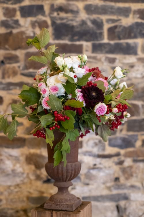 Elegant floral arrangement with roses, white flowers, and red berries in urn against stone wall at Domaine du Tertre Ychot,