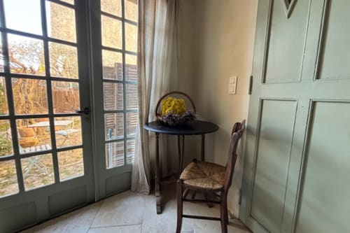 Cozy corner in Lourmarin courtyard apartment with small round table, wicker chair, yellow flowers, and garden view through