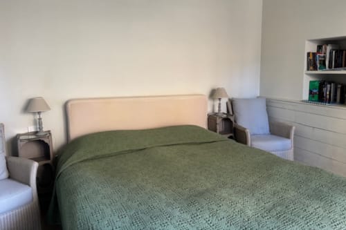 Bedroom in Lourmarin village apartment with green bedcover, cream headboard, bedside lamp, and wooden shelving