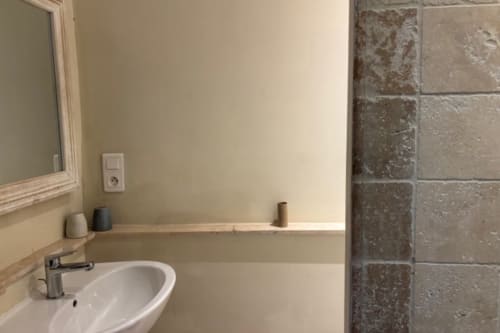 Modern bathroom sink with mirror in Lourmarin BnB apartment, gray tile shower wall visible