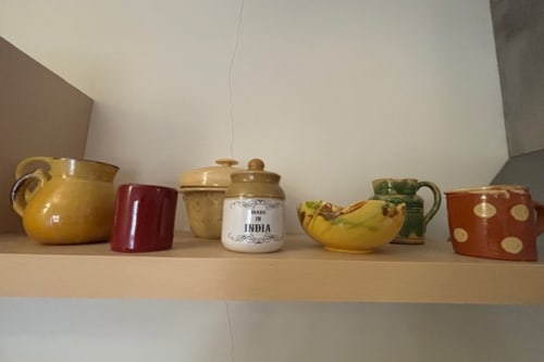 Decorative ceramic vessels and kitchenware displayed on shelf in Lourmarin apartment