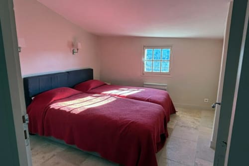 Bright bedroom in Lourmarin B&B with red bedding, pink walls, and window overlooking château views