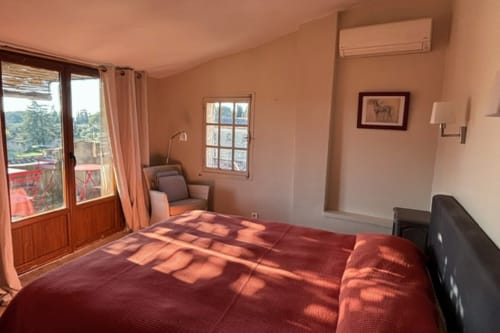 Sunny bedroom in Lourmarin B&B with red bed, balcony doors, mountain views, and sitting area