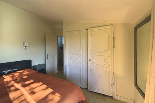 Bright bedroom in Lourmarin apartment with red bedding, white ornate wardrobe doors, and natural sunlight