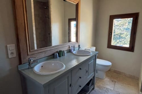 Modern bathroom with dual sinks, vanity storage, and toilet in Lourmarin apartment with mountain views through window