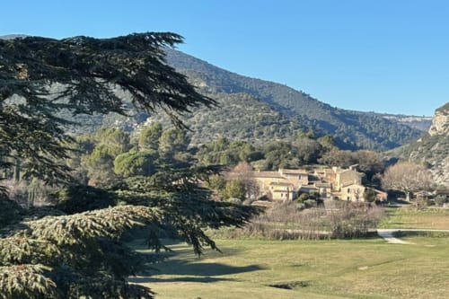 Lourmarin stone villa nestled in a valley with terraced gardens, forested mountains, and clear blue sky