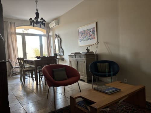 Spacious Music Room studio in Lourmarin with burgundy accent chair, dining table, and garden view through arched windows