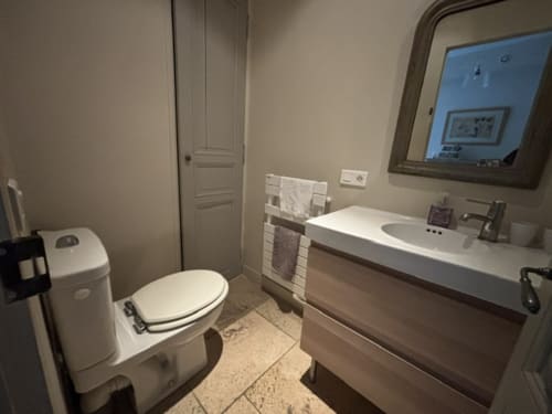 Modern bathroom in The Music Room at Ancienne Maison des Gardes, Lourmarin, featuring toilet, vanity sink, mirror, and tile