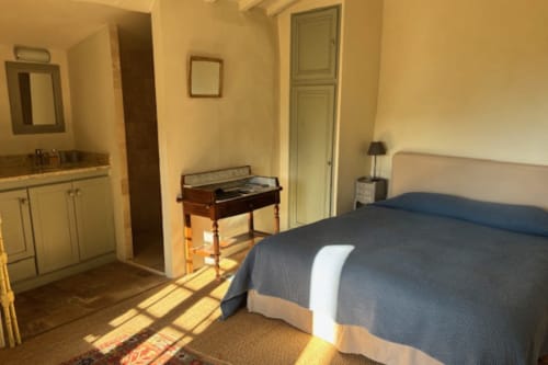 Spacious bedroom in Lourmarin B&B with queen bed, kitchenette, wooden antique desk, and garden views
