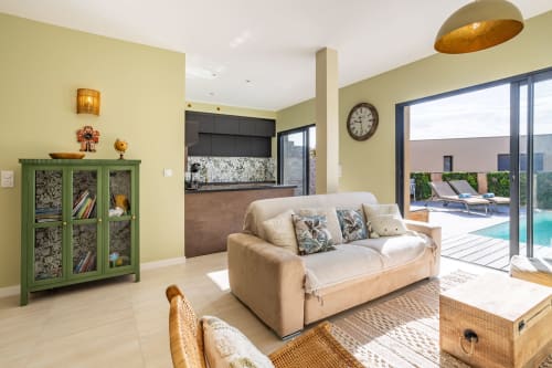Bright villa living room at Oia with cream sofa, pool view, green cabinet, and modern kitchen in Favone, managed by Corsu di Core conciergerie