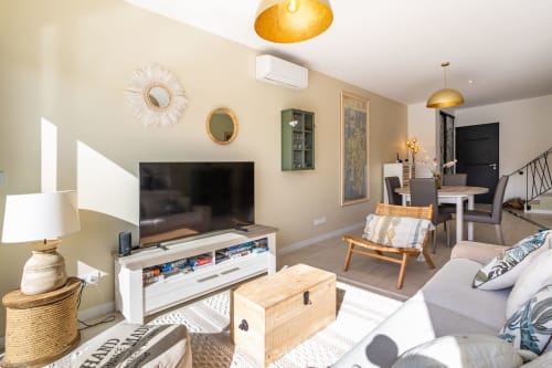 Modern villa living room at Oia Villa with flat-screen TV, comfortable seating, decorative mirrors, and golden pendant, managed by Corsu di Core conciergerie