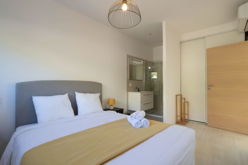 Modern bedroom in Villa Oia with gray upholstered bed, ensuite bathroom, and contemporary decor, managed by Corsu di Core