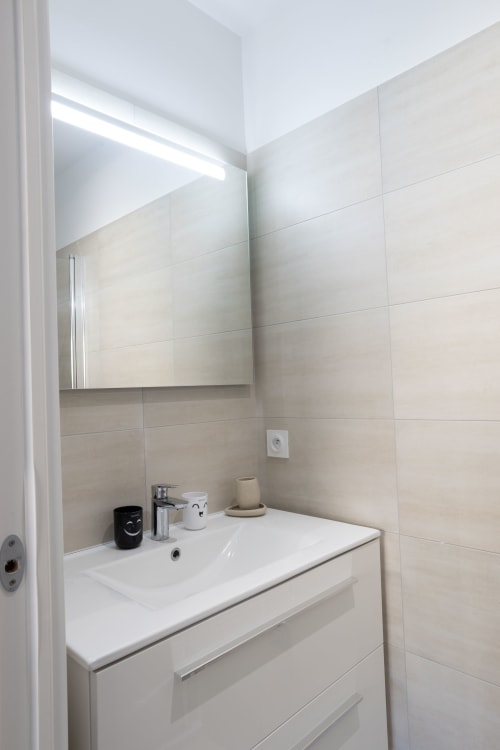 Modern bathroom at Villa Oia with white vanity, mirror and beige tiled walls, managed by Corsu di Core