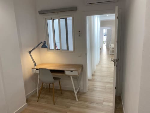 Espacio de trabajo moderno en Nerja Holiday Homes con escritorio de madera, silla, lámpara de escritorio y vista a través de puertas de vidrio al pasillo