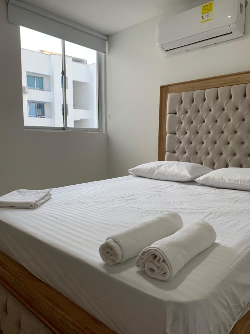 Habitación moderna en Olamar Living, Santiago de Tolú, con cabecera capitonada, ropa blanca, toallas enrolladas, aire acondicionado y ventana