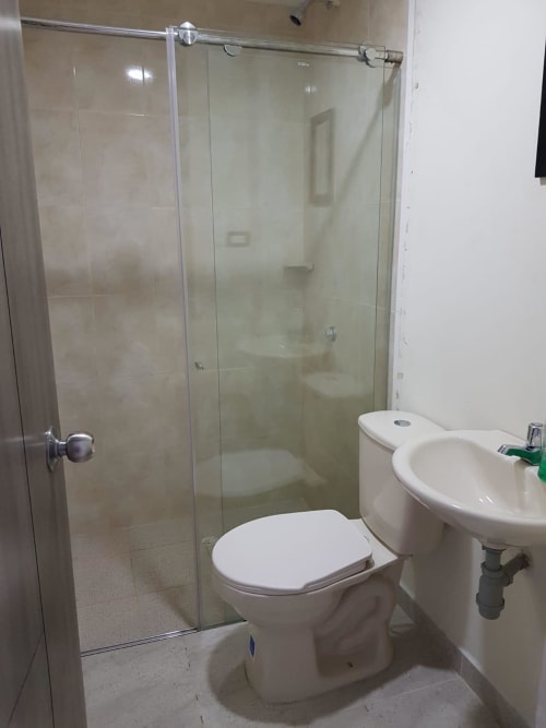 Baño moderno con cabina de ducha de vidrio, inodoro blanco y lavamanos pedestal en el hotel Olamar Living, Coveñas, Colombia