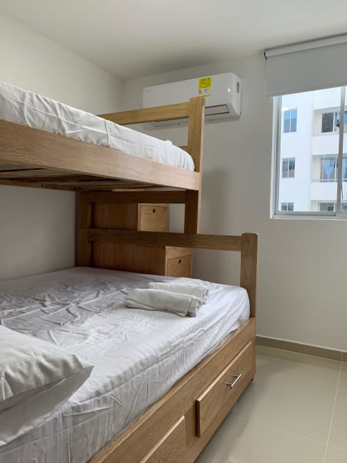 Camas literas de madera con sábanas blancas en habitación moderna del hotel Olamar Living en Coveñas, Colombia, con unidad de AC