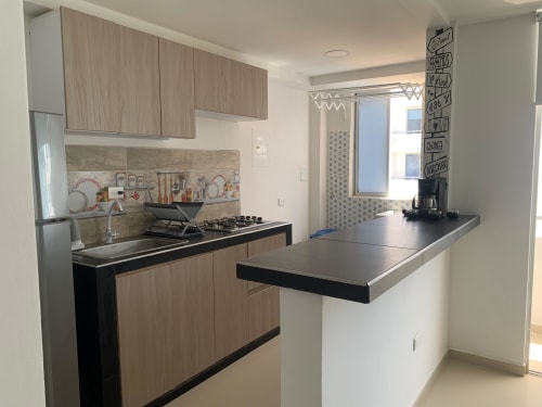 Cocina moderna con gabinetes de madera, encimeras negras, isla central y electrodomésticos de acero inoxidable en el apartamento Lake View Coveñas