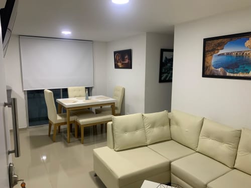 Sala de estar moderna en Olamar Living con sofá seccional color crema, mesa de comedor, pizarra y obras de arte costera