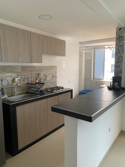 Cocina moderna con muebles de madera clara, encimera negra, estufa a gas e isla en Olamar Living, Santiago de Tolú