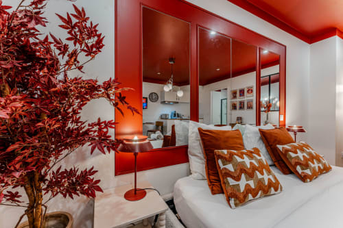 Modern red bedroom at Wellkhome Bordeaux with mirrored wall, white bed, patterned pillows, and Japanese maple plant