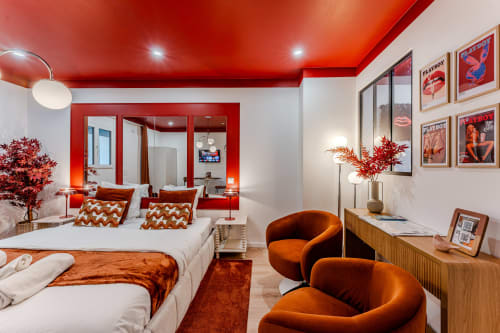 L'Écrin Rouge apartment in Bordeaux featuring red ceiling, white beds with orange pillows, orange armchairs, and Playboy