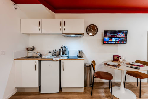 Modern apartment kitchen and dining area in Bordeaux with white cabinets, stainless steel appliances, wall-mounted TV, and