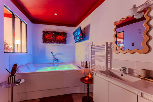 Modern bathroom with illuminated jacuzzi tub, red neon lips decor, and vanity sink in Bordeaux luxury apartment L'ÉCRIN ROUGE