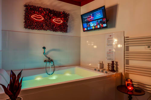 Modern luxury bathroom with illuminated Jacuzzi bathtub, neon lip wall art, and smart TV at Wellkhome Bordeaux
