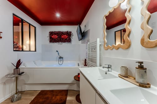 Modern luxury bathroom at Wellkhome Bordeaux with red ceiling, double vanity, soaking tub, and wavy wooden mirrors