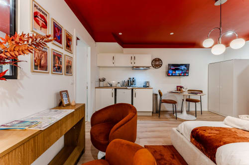 Modern red-themed studio apartment in Bordeaux with kitchenette, dining area, curved orange chair, and bed at Wellkhome