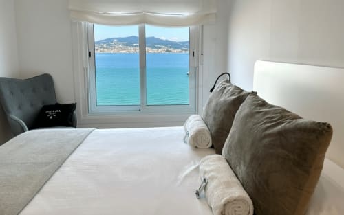 Dormitorio luminoso con vistas al mar, cama blanca, almohadas grises, apartamento en Baiona con vistas 