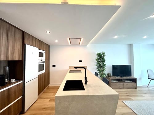 Cocina de planta abierta moderna y sala de estar en el apartamento Meiga do Mar, Baiona, con vistas al mar, mostrando encimeras blancas y madera