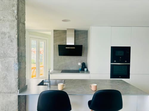 Moderna cocina con vistas al mar en apartamento de Baiona, armarios blancos, campana oscura, encimera de granito, taburetes negros