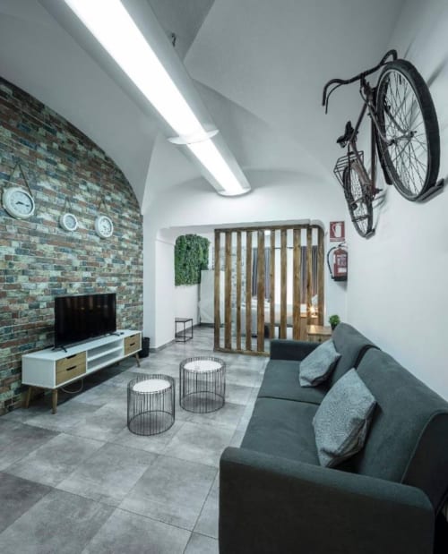 Sala moderna de apartamento en Mérida con pared de ladrillo, sofá gris, bicicleta montada, TV y divisores de madera