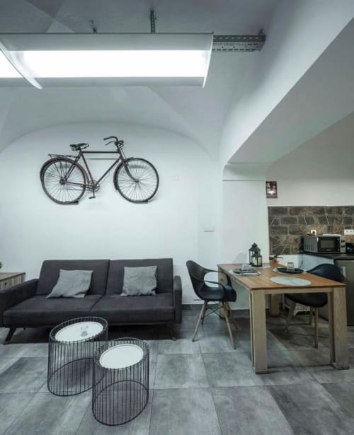 Apartamento estudio moderno en Mérida con sofá negro, mesa de comedor de madera, bicicleta de pared y techo con tragaluces