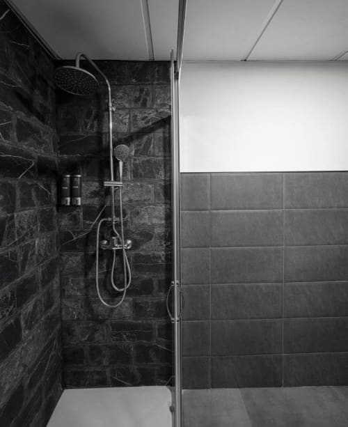 Moderno baño con ducha de mármol negro, alcachofas de lluvia y portátil en apartamento Gestyp-AT, Mérida