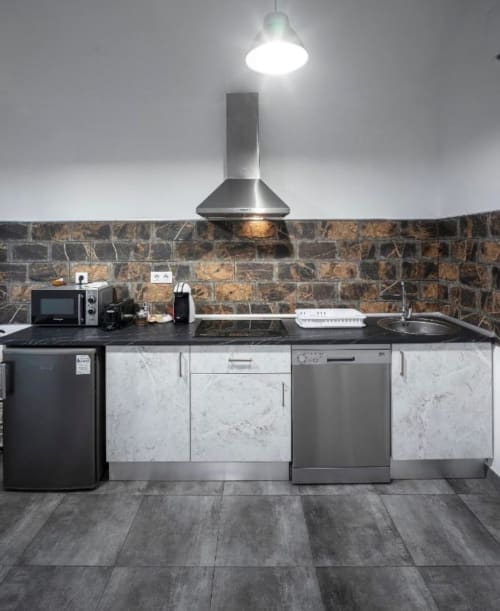 Cocina moderna con electrodomésticos de acero inoxidable, gabinetes efecto mármol, azulejos de piedra y luces colgantes en Mérida