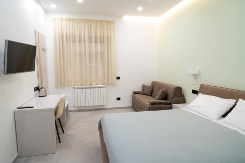 Camera da letto moderna a Museo19 Napoli con letto queen, TV, scrivania, poltrona marrone e vista sulla città