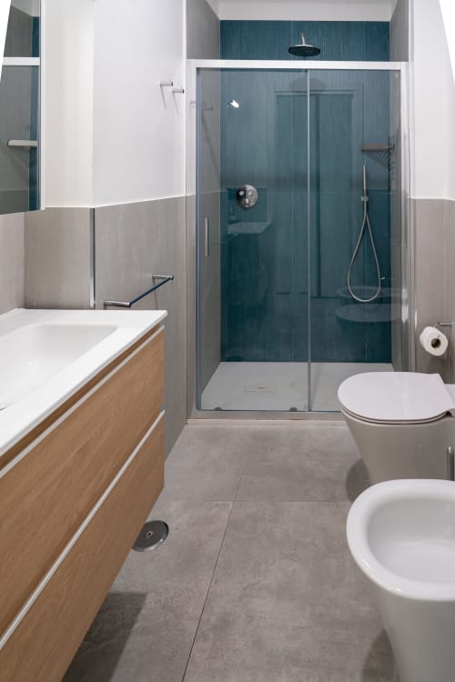 Bagno moderno al Museo19 Napoli con doccia in piastrelle color turchese, vanità in legno e pavimento in piastrelle grigie